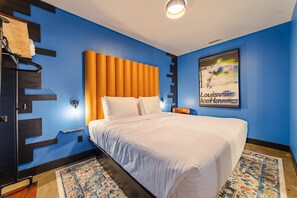 Ein Hotelzimmer mit einem großen Bett, einem Kopfteil, einer Wandleuchte, einem Poster und einem gemusterten Teppich.