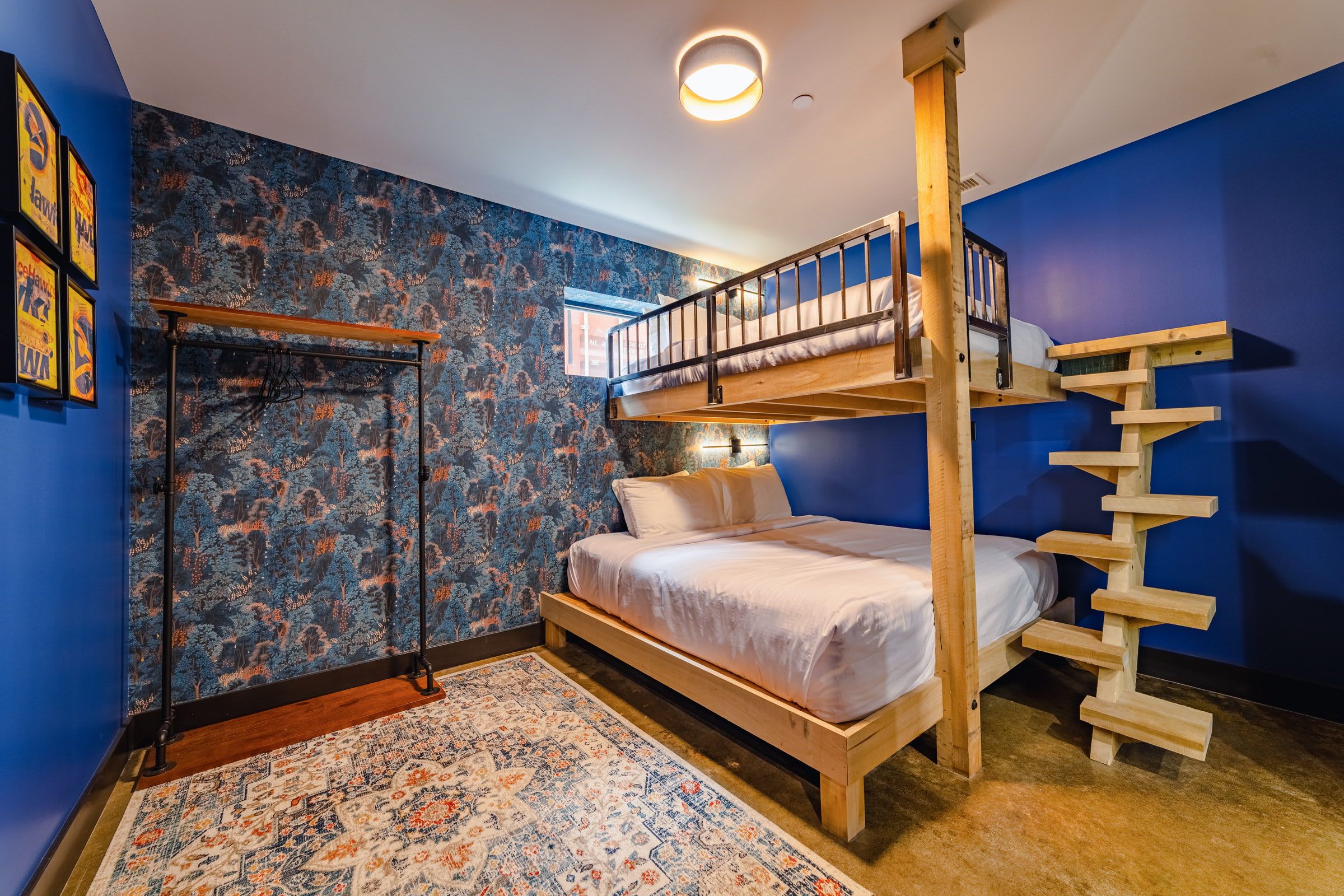 A room with a bunk bed, a wooden ladder, a patterned rug, and a wall with a forest-themed wallpaper.