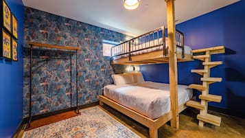 A room with a bunk bed, a wooden ladder, a patterned rug, and a wall with a forest-themed wallpaper.