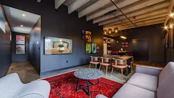 A modern living room with a large TV, artwork on the walls, and a dining area with chairs and a table.