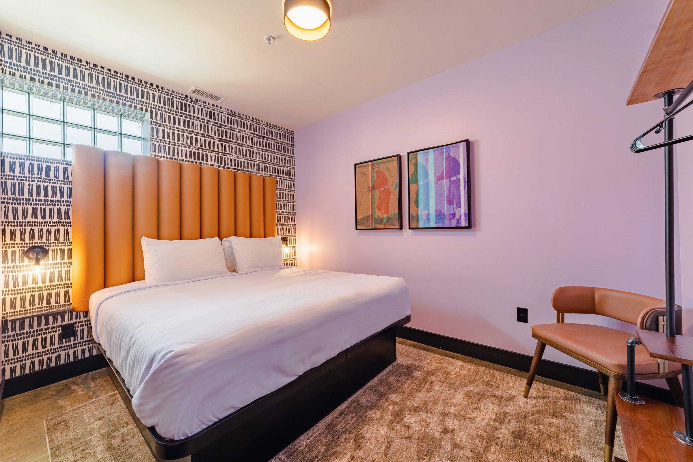 A modern bedroom with a large bed, a chair, and two framed artworks on the wall.
