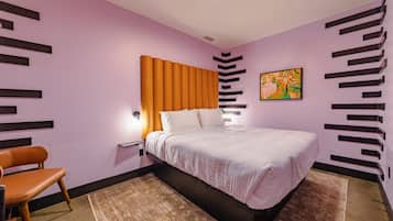 A modern bedroom with a bed, nightstand, chair, and artwork on the wall.