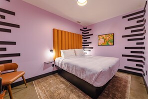 Ein modernes Schlafzimmer mit Bett, Nachttisch, Stuhl und einem Kunstwerk an der Wand.