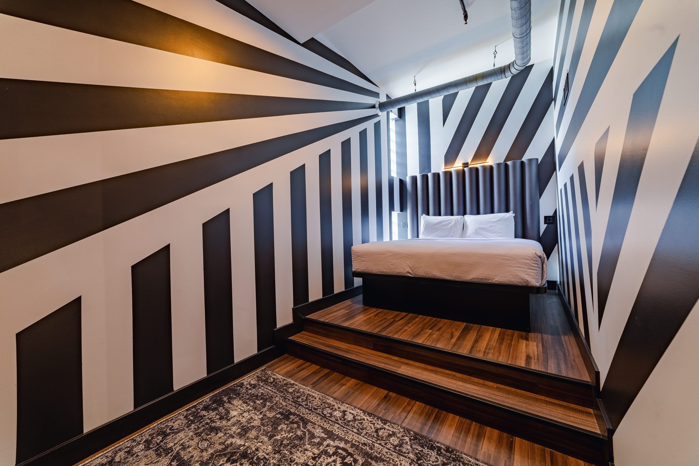 A narrow, striped room with a bed, a rug, and a ceiling vent.