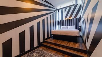 A narrow, striped room with a bed, a rug, and a ceiling vent.