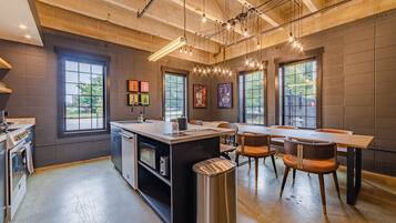 A modern kitchen with a central island, built-in oven, and a sink. There are large windows providing natural light and views of the outdoors.