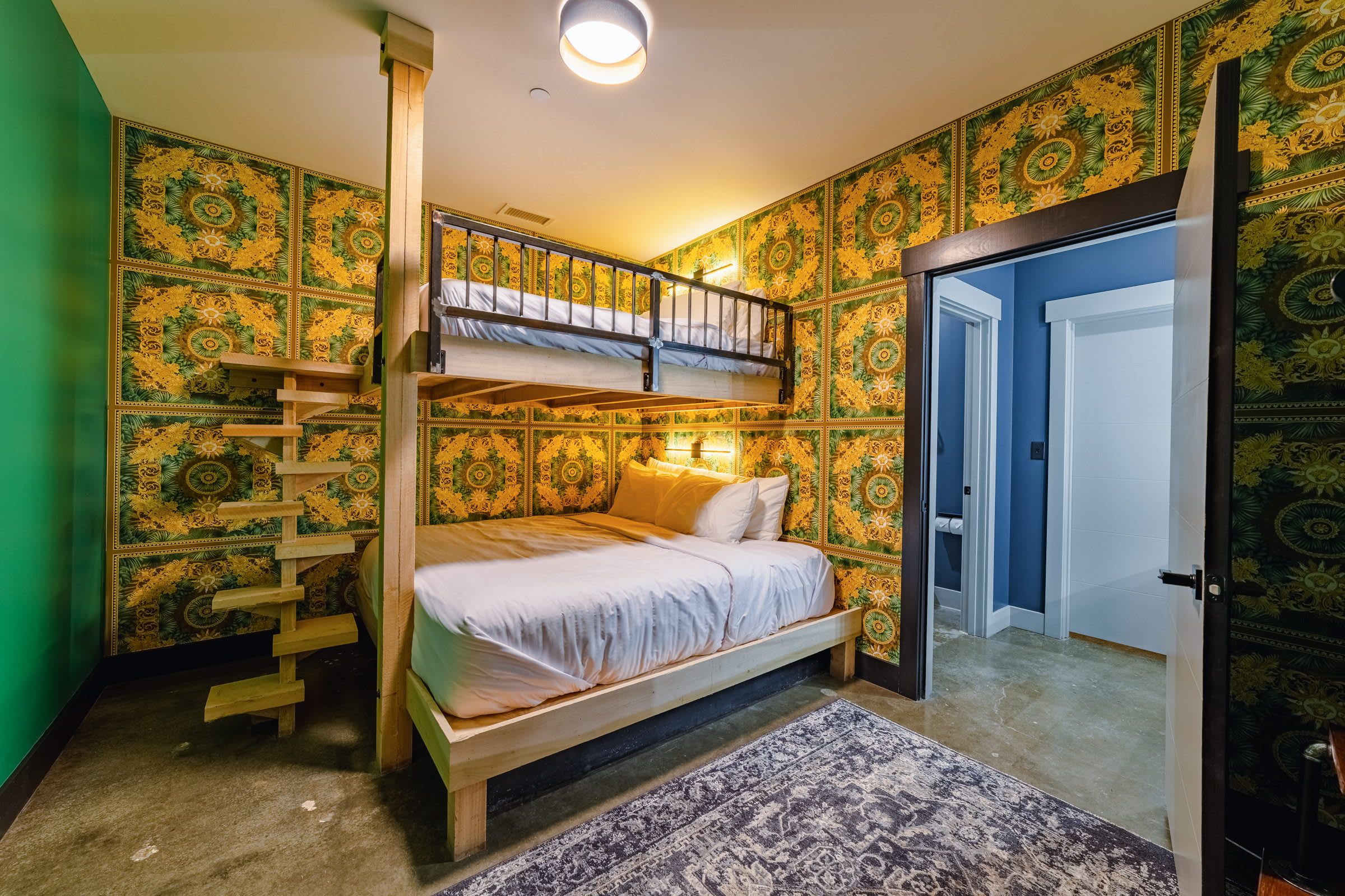 A room with a bunk bed, a wooden ladder, a patterned wall, and a door leading to another room.