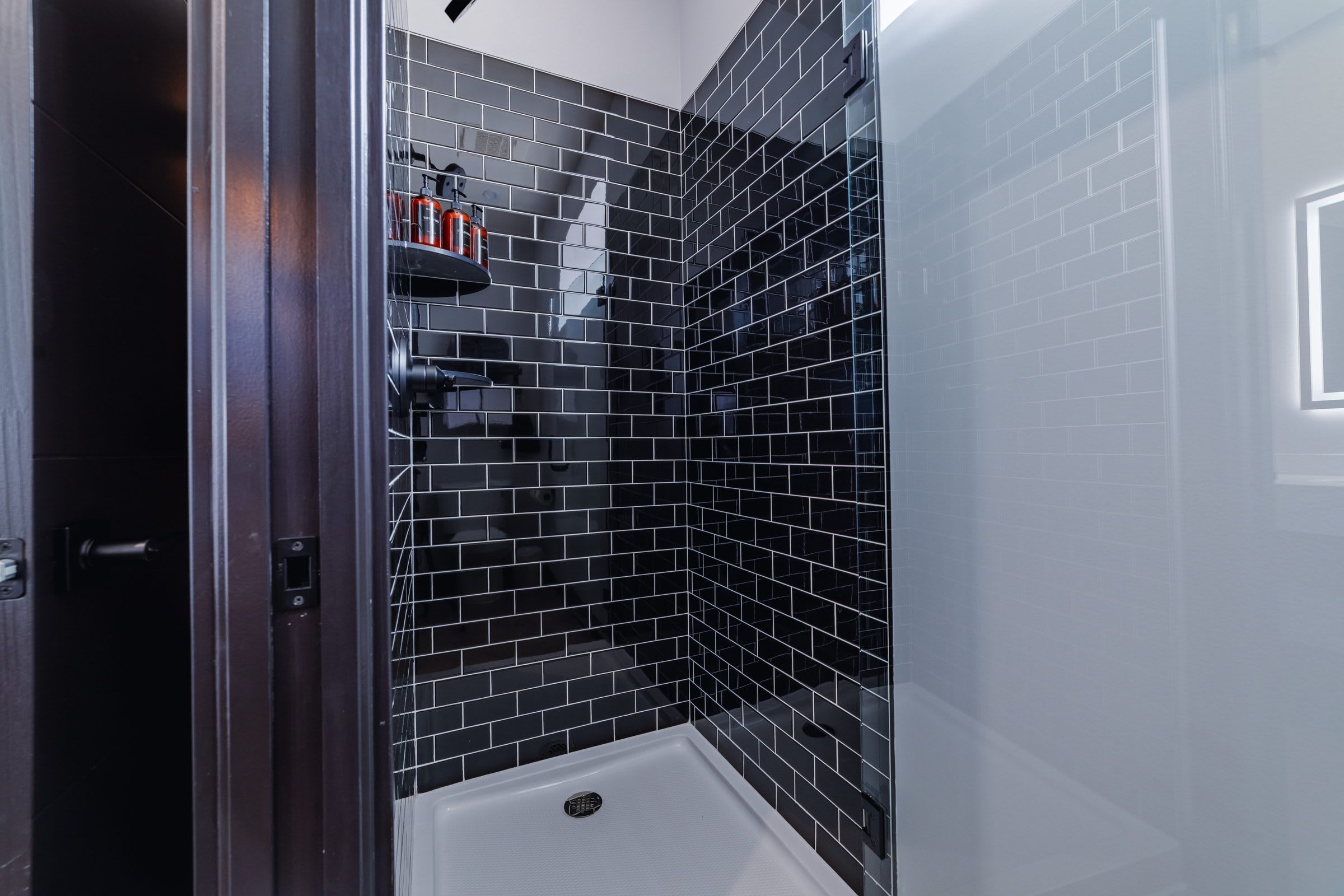 Une salle de bain moderne avec des murs recouverts de carreaux noirs, un espace douche blanc et une porte de douche en verre.