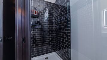 Une salle de bain moderne avec des murs recouverts de carreaux noirs, un espace douche blanc et une porte de douche en verre.