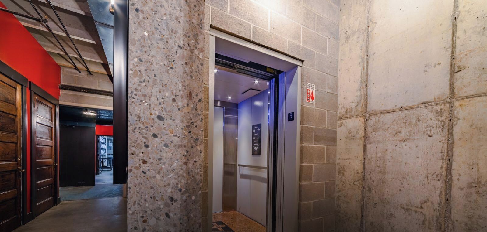 Um elevador com uma placa indicando o andar, um sinal de segurança contra incêndio e um corredor com parede vermelha e uma porta.