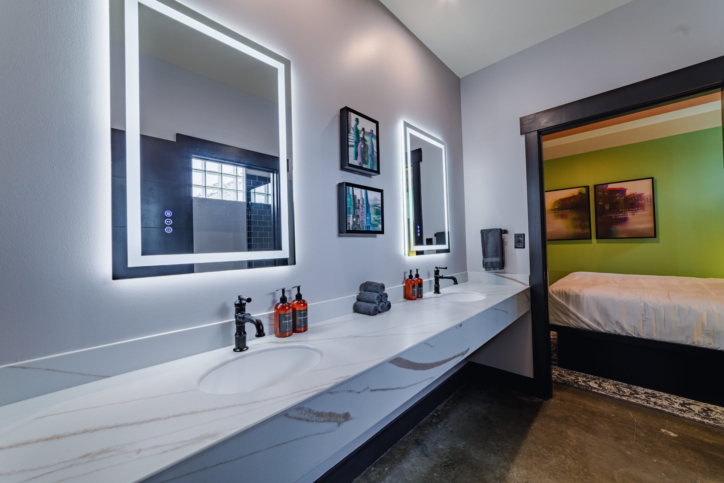 A modern bathroom with two sinks, a large mirror, and a bed with a green wall.