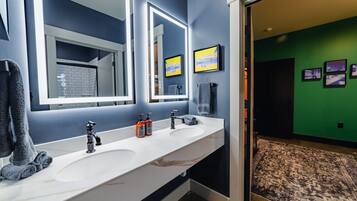 A modern bathroom with two sinks, a large mirror, and a green wall with framed pictures.