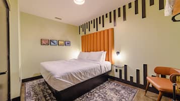 A hotel room with a bed, a chair, a rug, a wall with pictures, and a ceiling light.