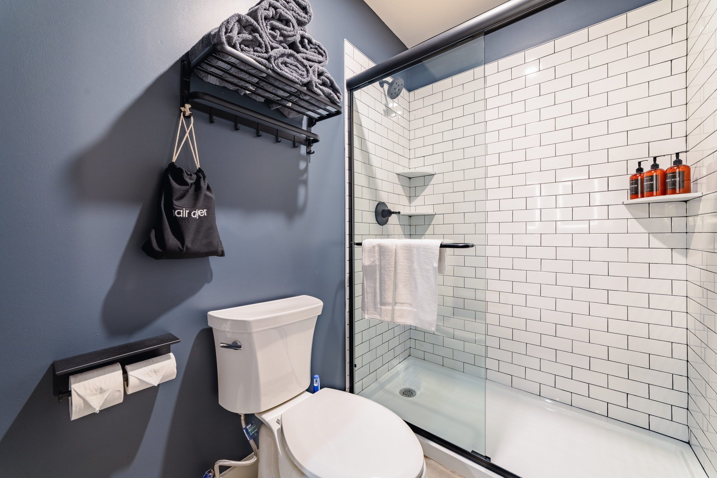 Een badkamer met toilet, een glazen douchecabine, een handdoekrek en een plank met toiletartikelen.