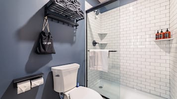 Een badkamer met toilet, een glazen douchecabine, een handdoekrek en een plank met toiletartikelen.