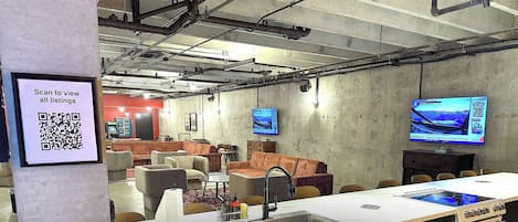 Un espace de détente moderne avec des canapés, une longue table et un code QR permettant de consulter les annonces.