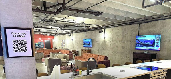 Ein moderner Lounge-Bereich mit Sofas, einem langen Tisch und einem QR-Code zum Anzeigen von Angeboten.