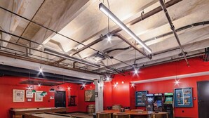Une pièce aux murs rouges, dotée de tuyaux industriels apparents au plafond, d’une table de billard et de machines de jeux.