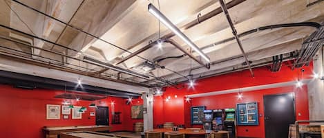A room with red walls, exposed ceiling pipes, and a pool table.
