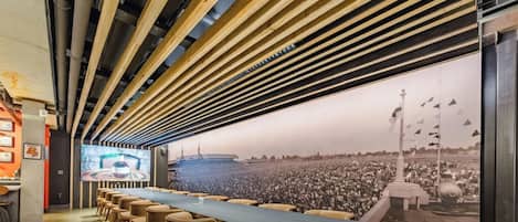 Un salón de conferencias con una larga mesa, sillas y una pantalla grande que muestra una multitud.