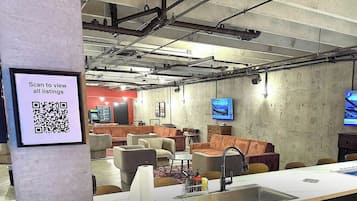 A modern lounge area with sofas, a long table, and a QR code for viewing listings.