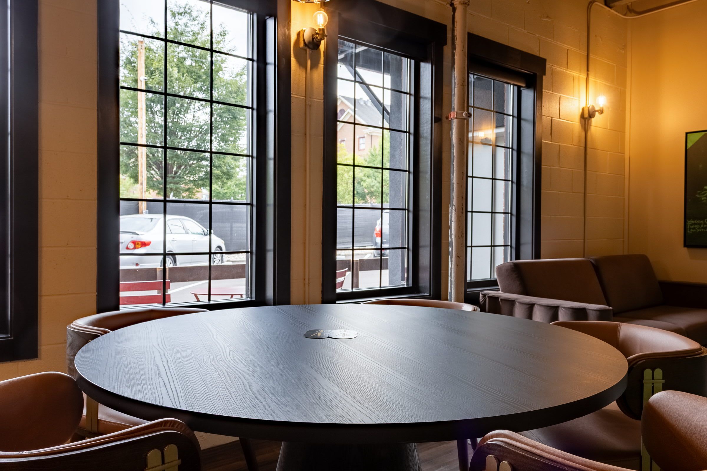 A round table with chairs in a room with large windows and a view of the street outside.