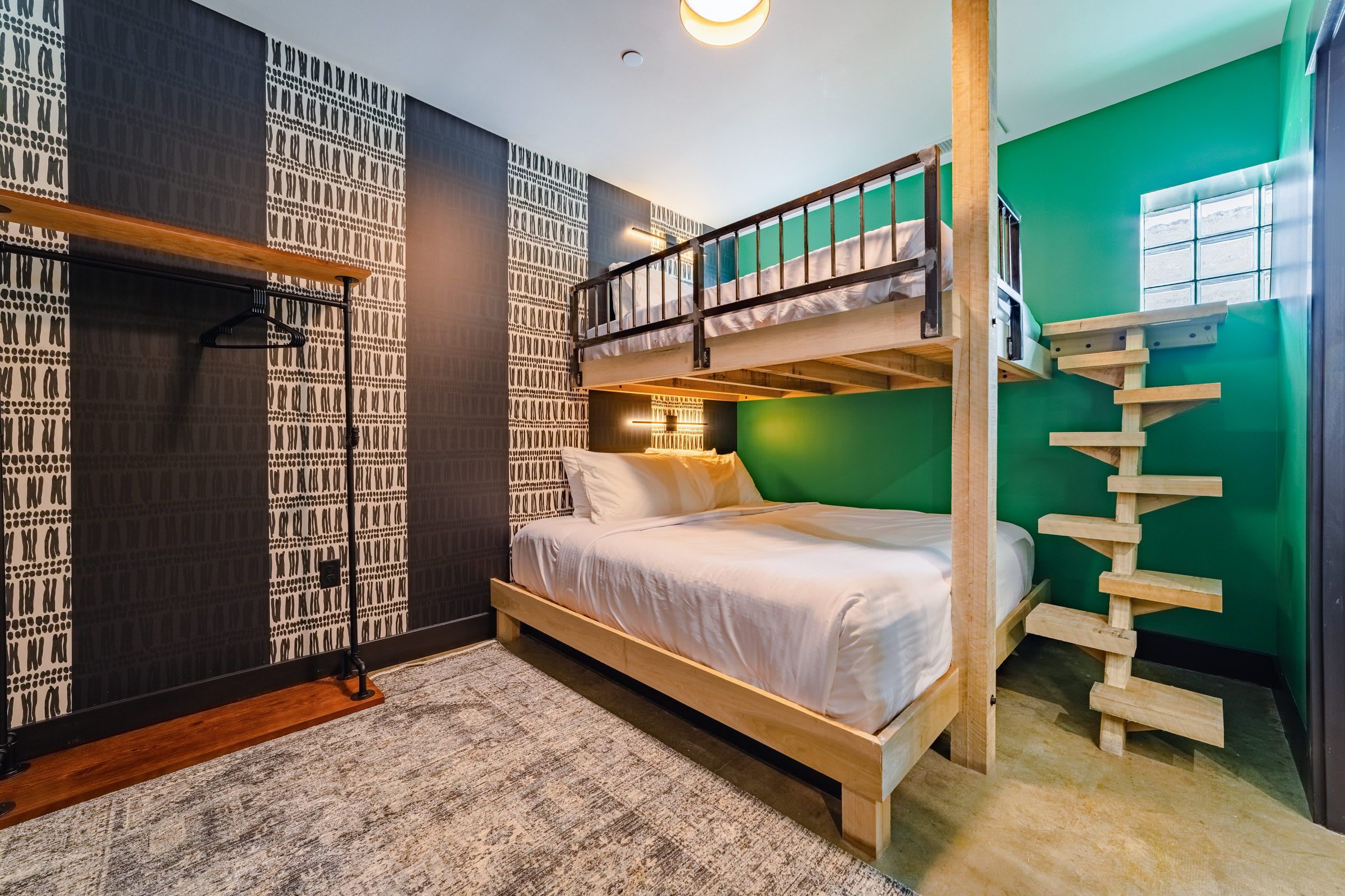Une chambre avec des lits superposés, un mur vert, un mur à motifs et un plancher en bois.