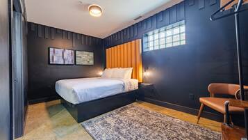 A modern bedroom with a bed, a chair, a rug, and artwork on the wall.
