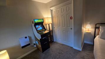 Quarto de hotel com console de jogos, porta, luminária e cama.