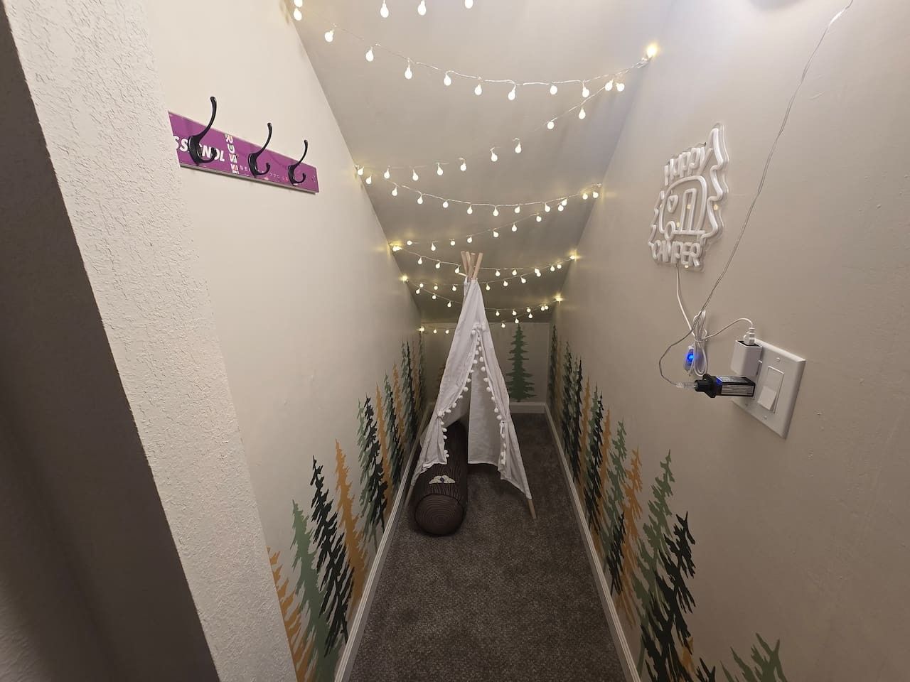 Um corredor estreito com uma tenda tipo dossel, luzes de Natal e uma tomada na parede.