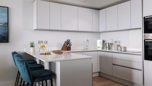 Een moderne keuken met witte kastjes, een centraal eiland, barkrukken en een koffieapparaat.