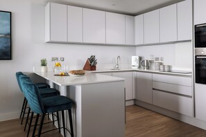 A modern kitchen with white cabinetry, a central island, bar stools, and a coffee machine. - Liner Apartment 44 - 3 Bedroom - Fourth Floor (Falmouth)