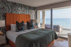 A hotel room with a large bed, a view of the sea, and a patterned wall. - Liner Apartment 44 - 3 Bedroom - Fourth Floor (Falmouth)