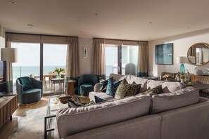 A modern living room with a large sofa, armchairs, and a dining area. - Liner Apartment 44 - 3 Bedroom - Fourth Floor (Falmouth)
