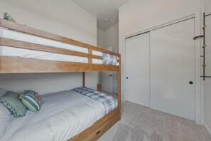 Ein Etagenbett mit Holzrahmen, weißer Bettwäsche und zwei Kissen. Im Hintergrund ist eine weiße Tür mit Griff erkennbar.