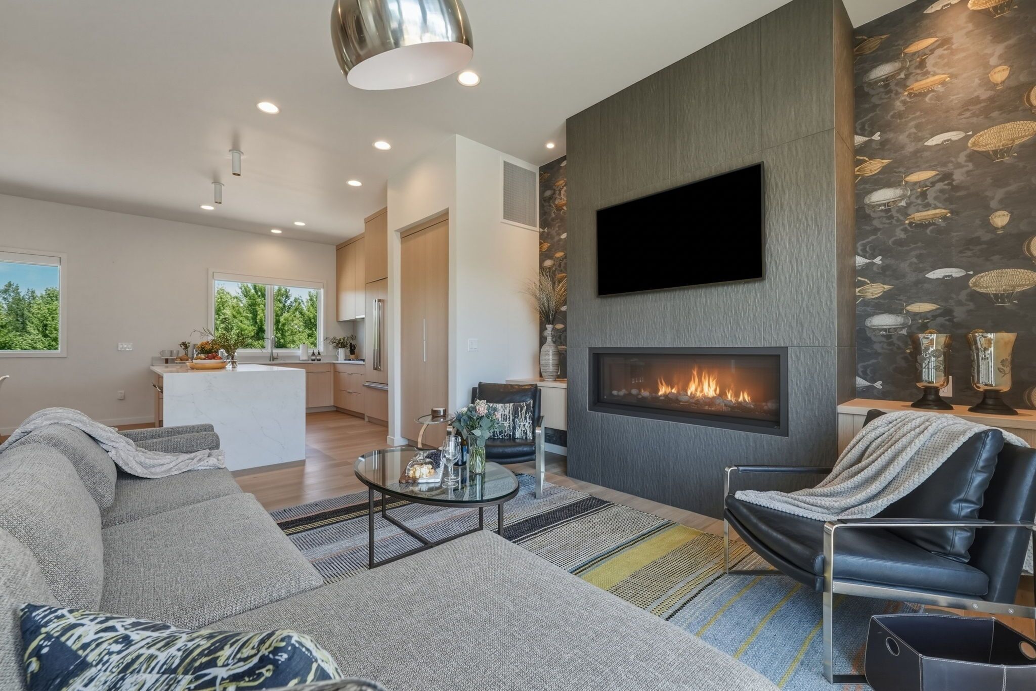 A modern living room with a fireplace, a sofa, a recliner, and a television mounted on the wall.