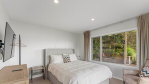 Um quarto com uma cama, uma escrivaninha, uma cadeira e uma janela com vista para o verde.