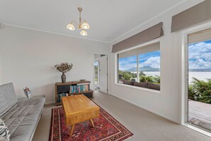Ein Wohnzimmer mit einer Couch, Couchtisch, Bücherregal und großen Fenstern mit Blick ins Freie.