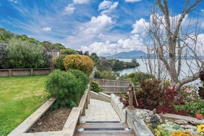A wooden staircase leading to a garden with a view of a lake and mountains. - Lakeside Lookout - Acacia Bay Holiday Home (Taupo)
