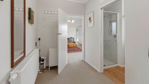 A hallway with a radiator, a mirror, a door leading to a bathroom with a shower, and a small table with books.