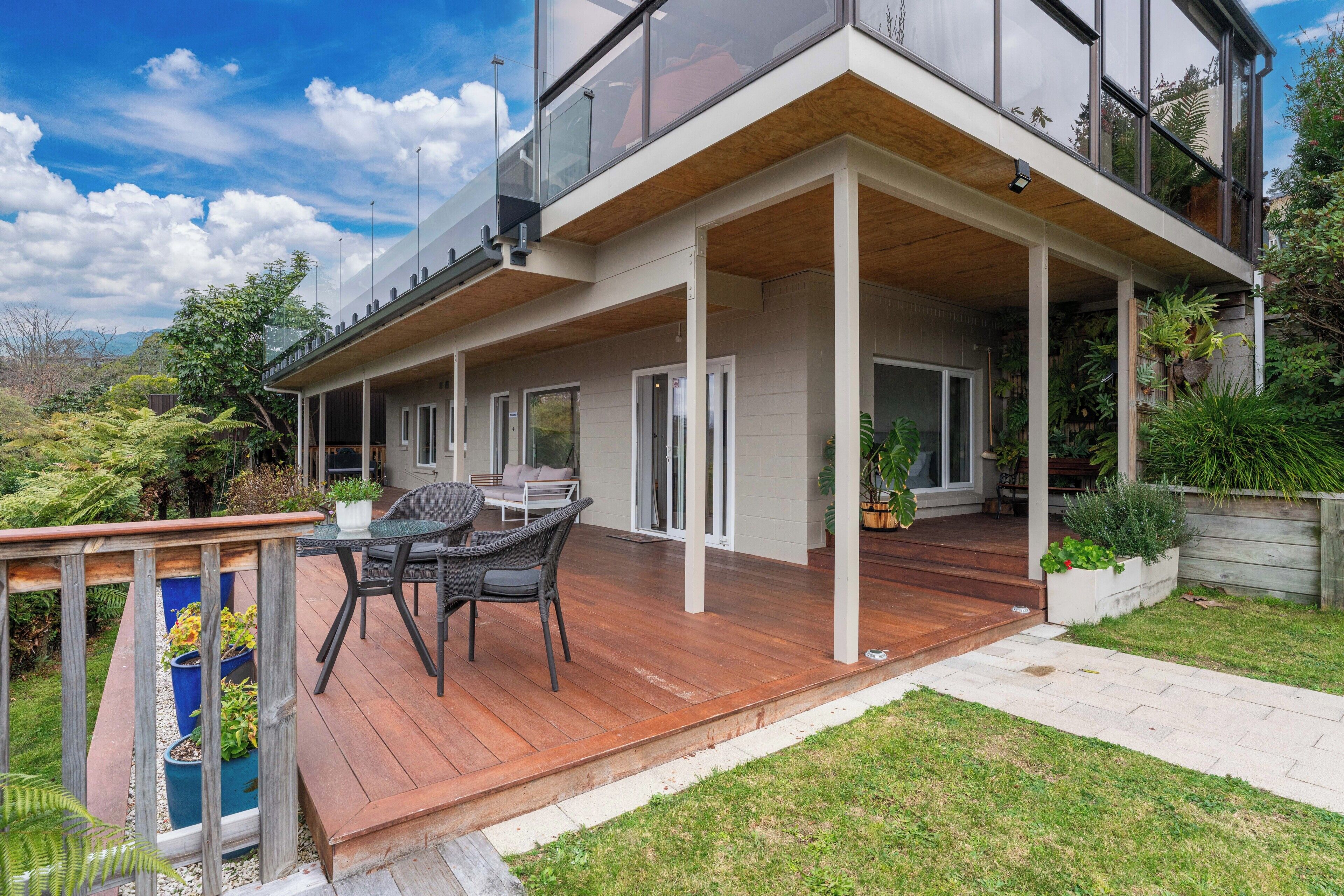 Een modern huis met twee verdiepingen, een houten terras, zitplaatsen buiten en uitzicht op het omliggende landschap.
