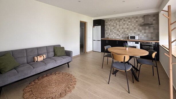 A modern living space with a sofa, dining table, chairs, and a kitchen area with appliances. - La Mimosa Apartment 2607 (San Miguel de Meruelo)