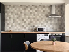 A modern kitchen with a tiled backsplash, a microwave, a stove, a dishwasher, and a round wooden table with chairs. - La Mimosa Apartment 2607 (San Miguel de Meruelo)
