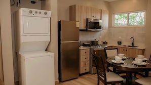A compact kitchen with a washing machine, refrigerator, microwave, stove, and dining area with chairs and a table set for four. - Luxury Apartment with Breathtaking Mountain Views | Pet-Friendly (Alto Boquete)
