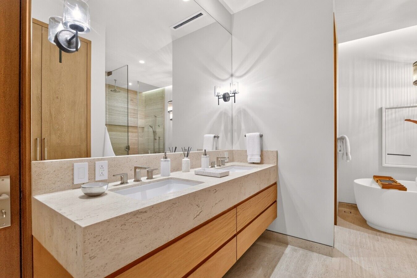 A modern bathroom with a large mirror, two sinks, a bathtub, and a shower.
