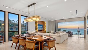 Een moderne woonkamer met een eethoek, grote ramen en uitzicht op zee.