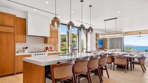 Een moderne keuken met een centraal eiland, een eethoek met rieten stoelen en uitzicht op de oceaan.