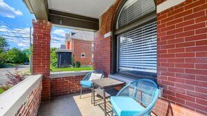 En overdækket terrasse med murstensvæg, et bord, to stole og et vindue med persienner.