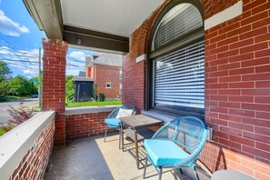 A covered patio with a brick wall, a table, two chairs, and a window with blinds. - 3BR Victorian in Old Oaks, near German Village (Columbus)