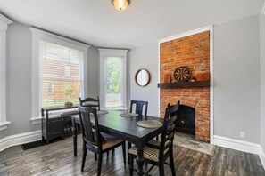 A dining room with a brick fireplace, a dartboard, and a window with blinds. - 3BR Victorian in Old Oaks, near German Village (Columbus)
